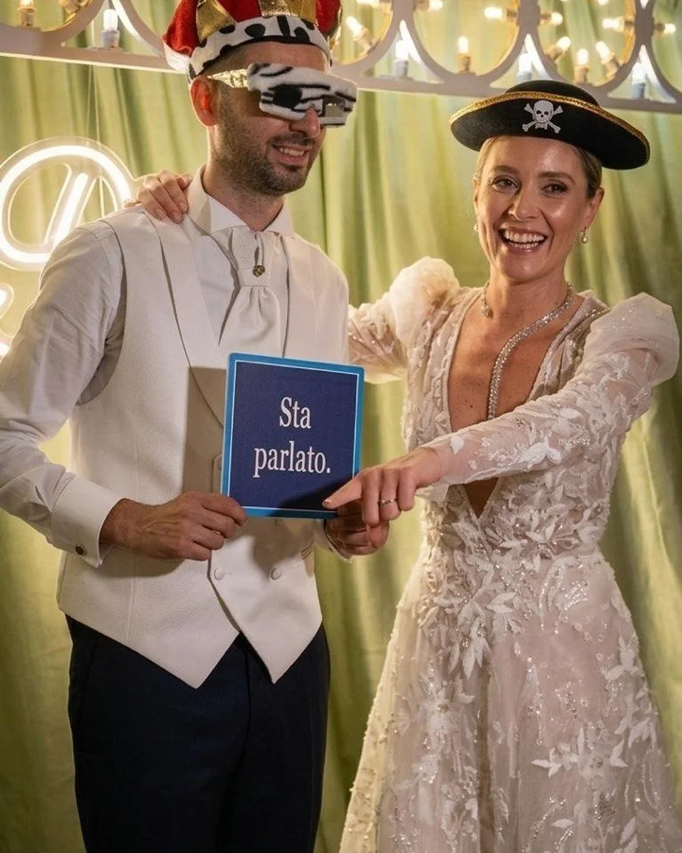 Sposi al Photo Booth con cappelli e cartello «Sta parlato.»